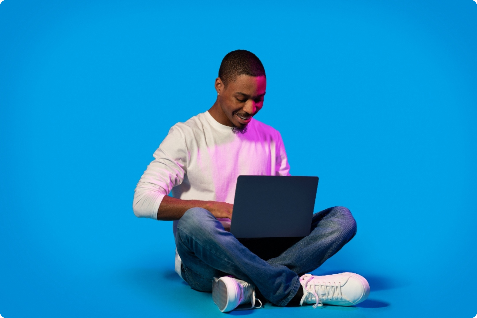 black-man-using-laptop-sitting-on-blue-in-neon-li-2023-11-27-05-13-02-utc 1